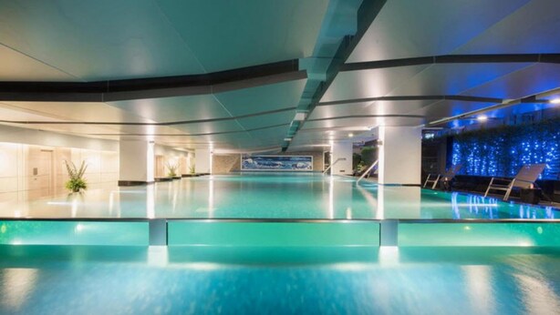 An indoor swimming pool with clear water, surrounded by lounge chairs and a tiled wall with a blue design. - Qiss Residence by Bliston (Bangkok)
