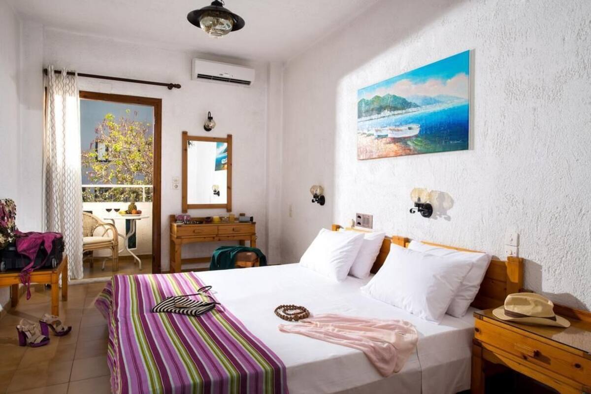 A bedroom with a bed, a dresser, a nightstand, a window with a view, and a painting on the wall.