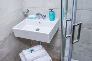 A bathroom with a white sink, a glass shower enclosure, and a towel with a star design. - Floral Hotel (Hersonissos)