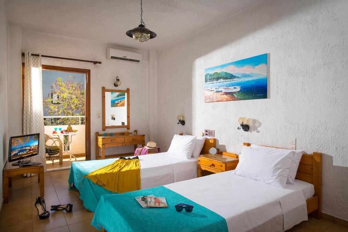 A hotel room with two beds, a TV, a balcony with a view, and a painting on the wall.