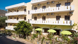 A multi-story hotel with balconies, outdoor seating, and a stone wall. - Floral Hotel (Hersonissos)