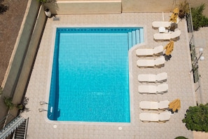 A rectangular swimming pool with a tiled edge, surrounded by lounge chairs and umbrellas. - Floral Hotel (Hersonissos)