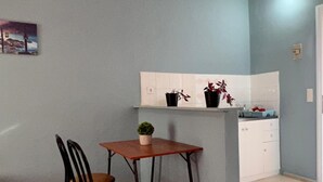 Un petit coin repas avec une table et deux chaises, une plante en pot et un plan de travail de cuisine avec des placards et un évier.