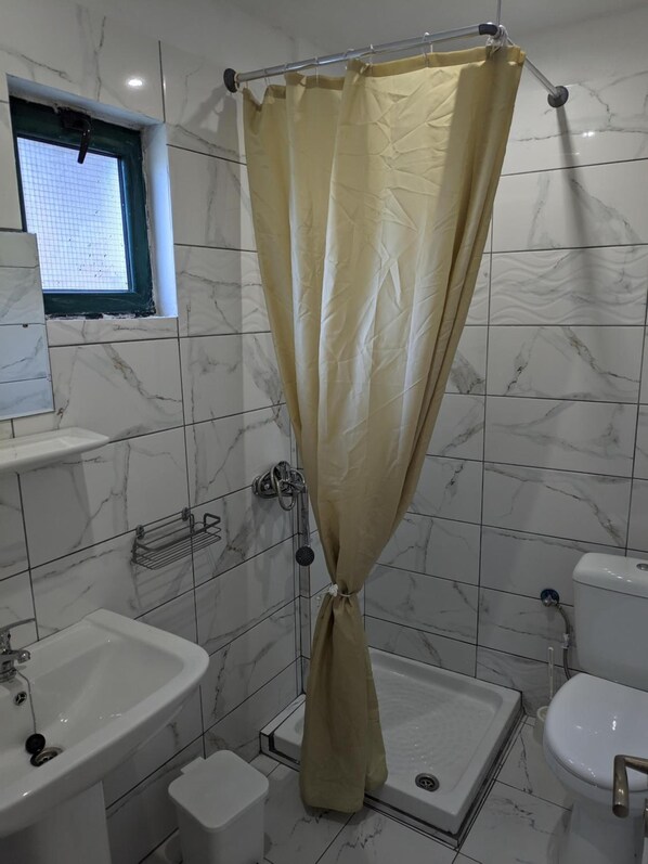 A bathroom with a shower curtain, a window, a sink, a toilet, and a bidet. - Elena Pool Apartments (Corfu)