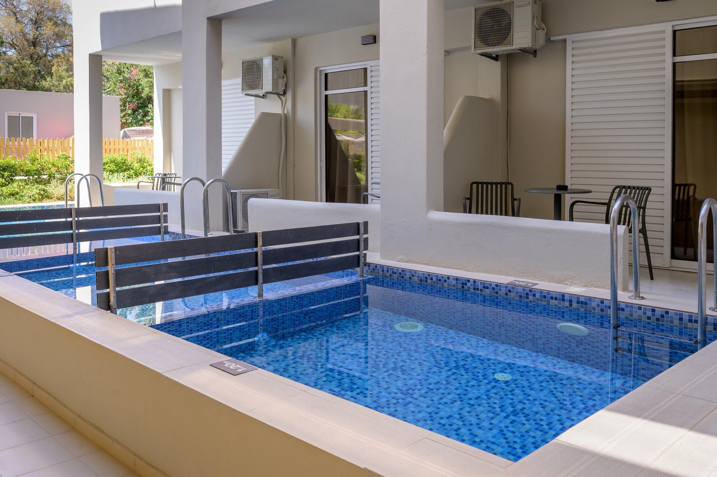 A rectangular indoor swimming pool with blue mosaic tiles, surrounded by a white deck.
