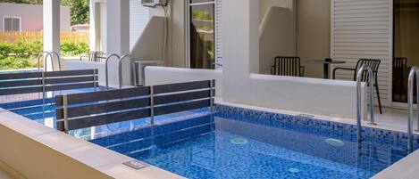 A rectangular indoor swimming pool with blue mosaic tiles, surrounded by a white deck.
