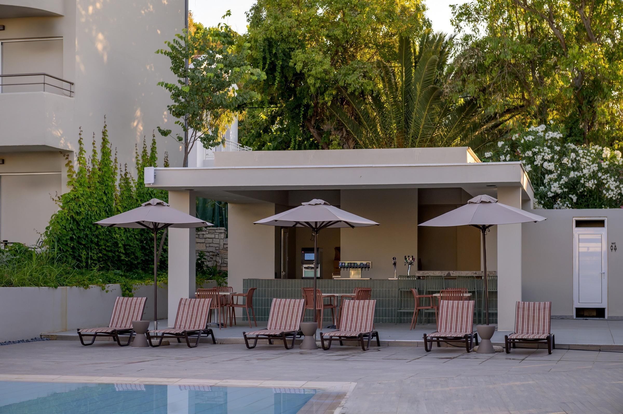 Un área junto a la piscina con sillones de descanso y sombrillas, un bar y una piscina.