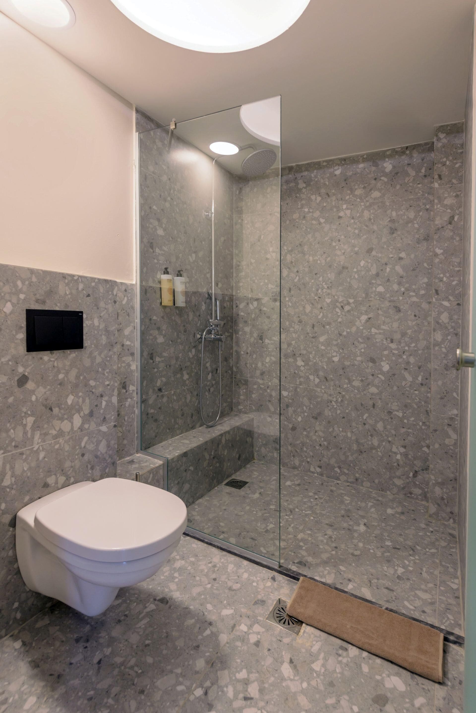 A modern bathroom with a glass-enclosed shower, a toilet, and a marble-tiled floor.