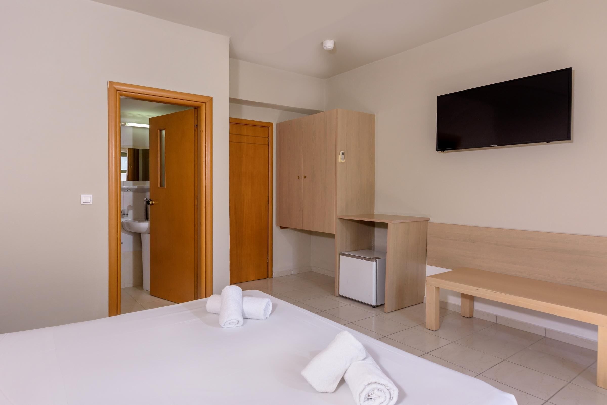 A hotel room with a bed, a bench, a TV, a wardrobe, and a small cabinet.