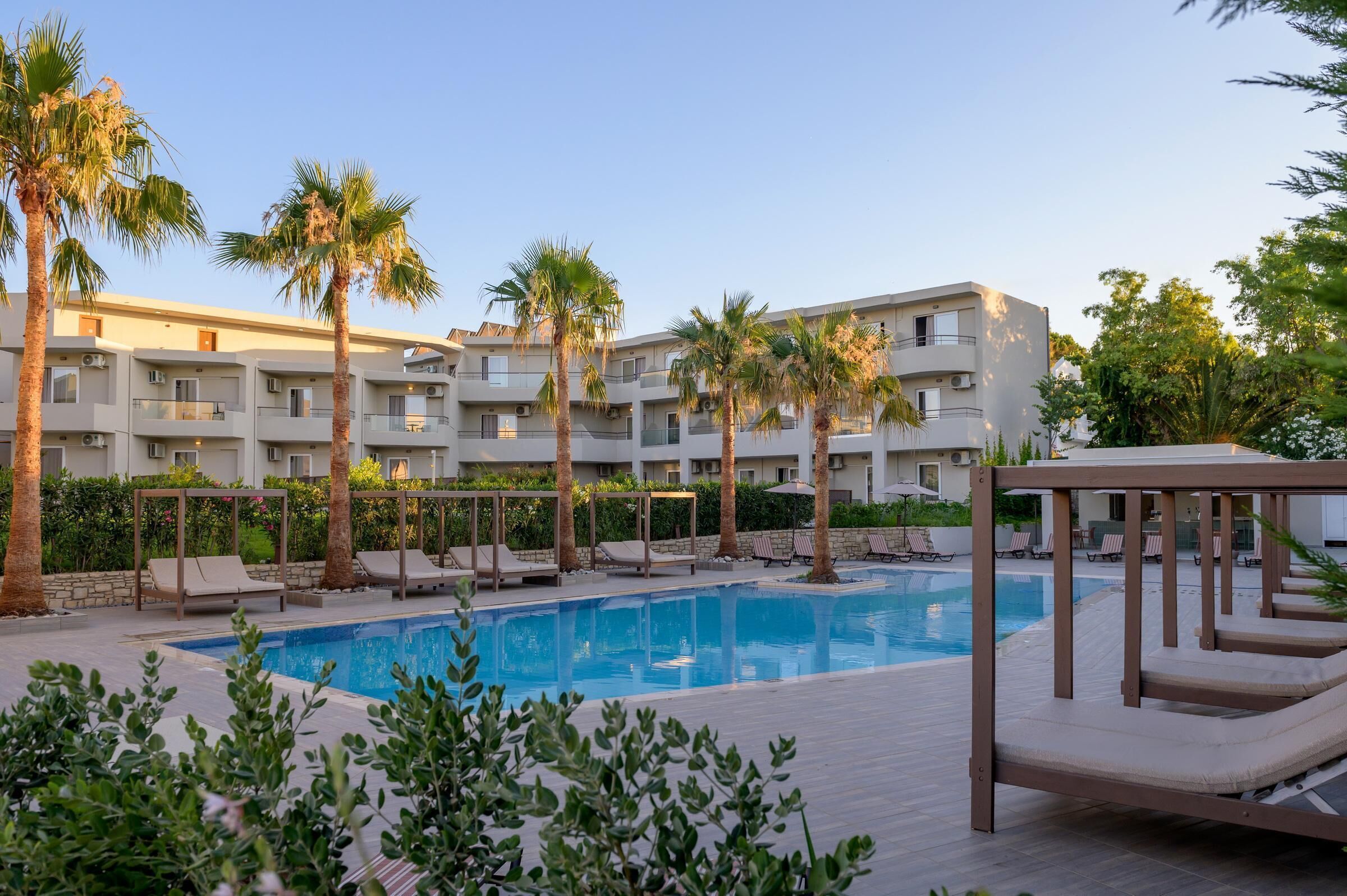 A swimming pool with lounge chairs and palm trees, surrounded by a building with balconies.