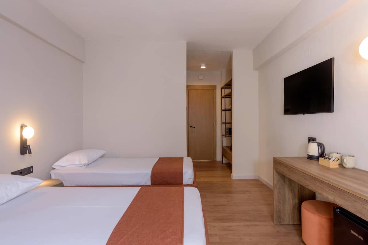 A hotel room with two beds, a desk with a television, and a coffee maker.