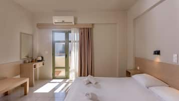 A hotel room with a bed, bedside tables, a desk, a chair, an air conditioning unit, and a view through the door.