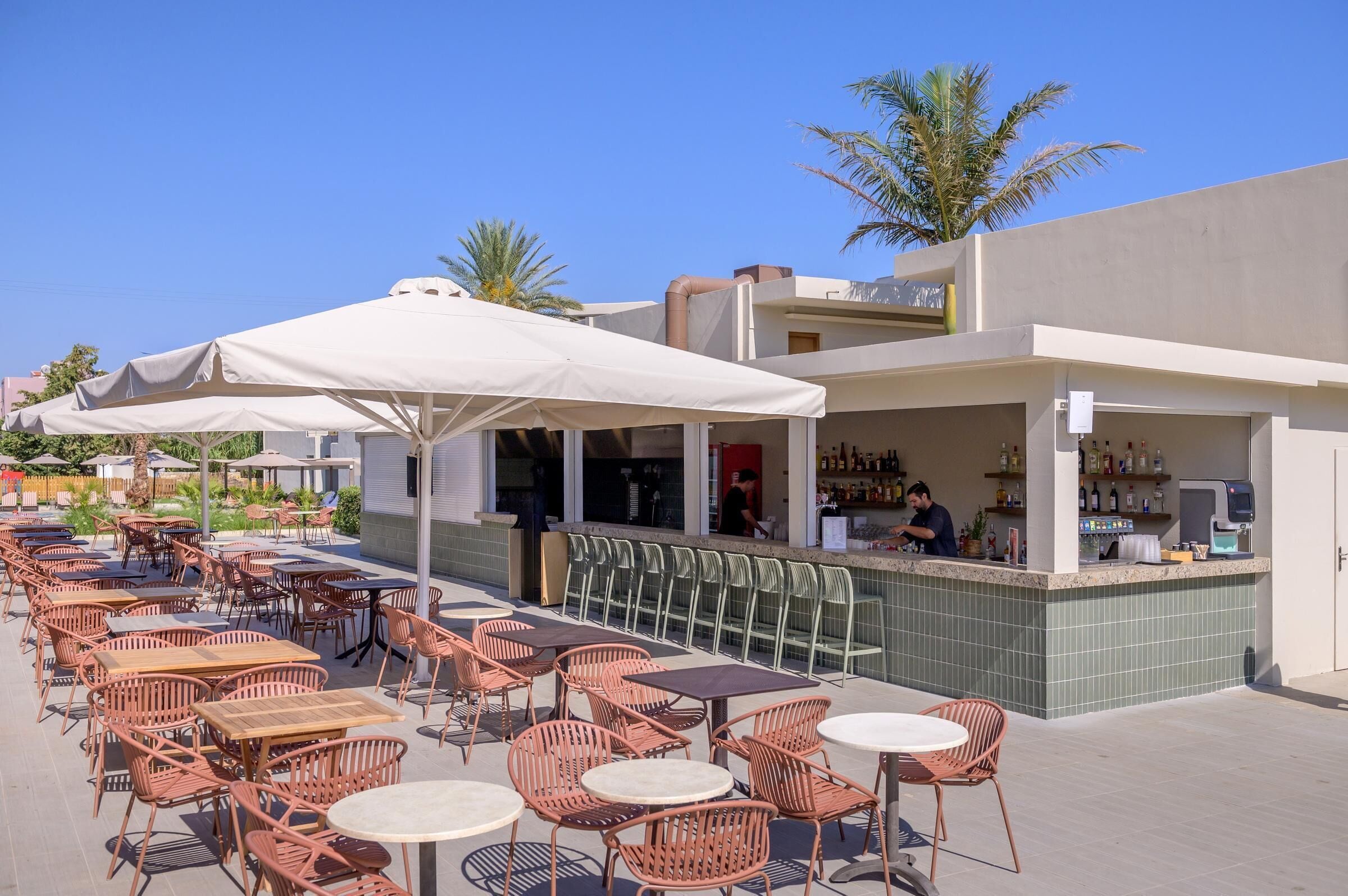 An outdoor seating area with tables and chairs, a bar with a tiled counter, and a palm tree in the background.