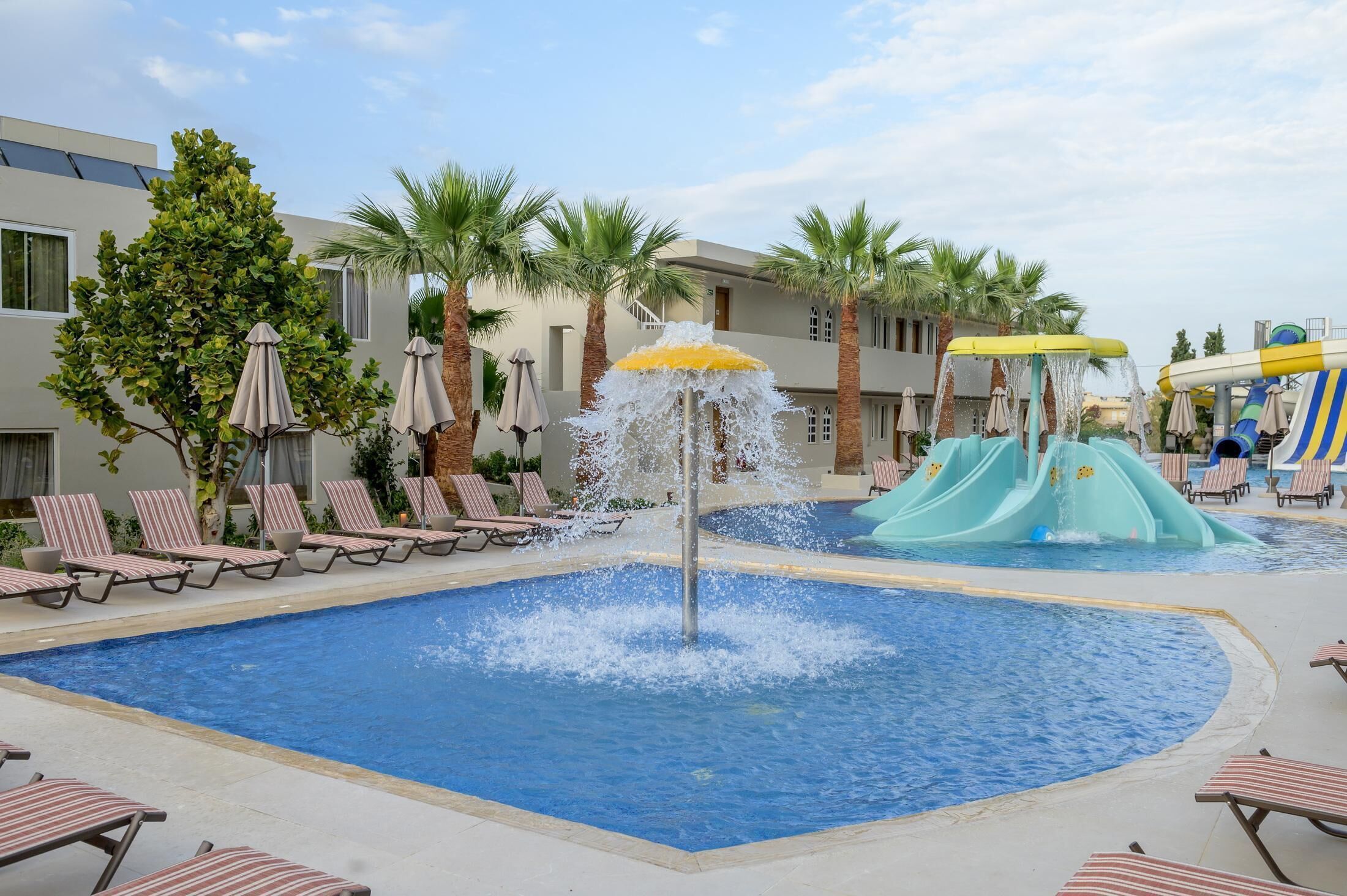 A pool area with lounge chairs, a water feature, and a children's water slide.