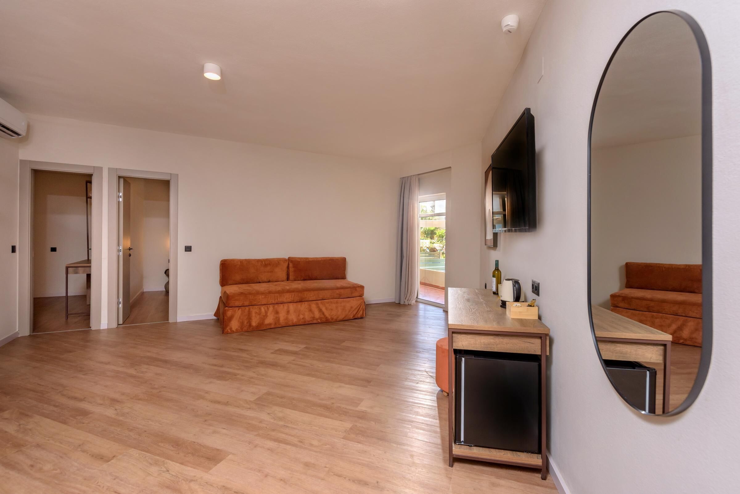 Un salón espacioso con suelo de madera, un sofá, un televisor montado en la pared y un espejo grande.