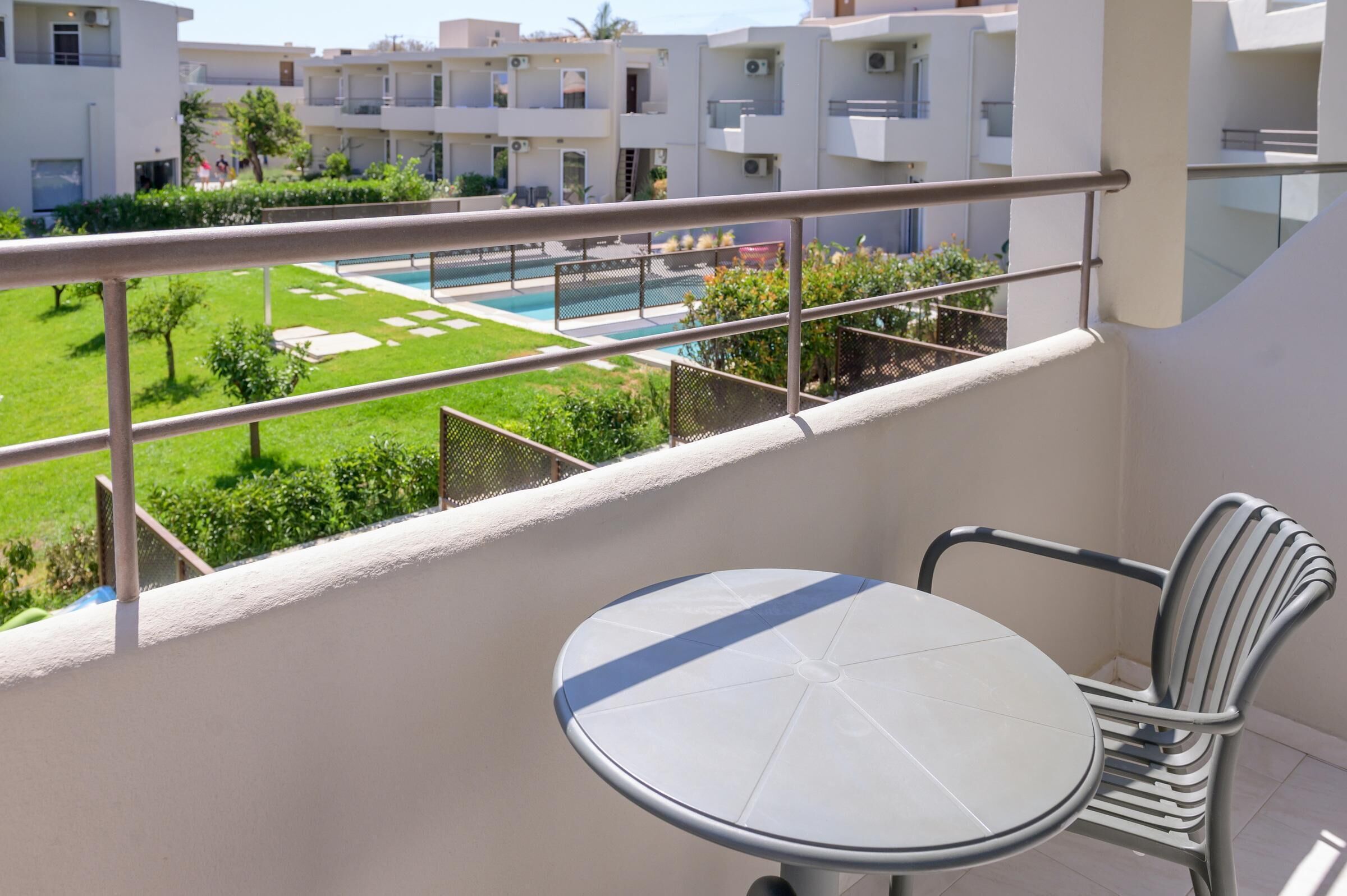 A balcony with a table and chair, overlooking a swimming pool and greenery.