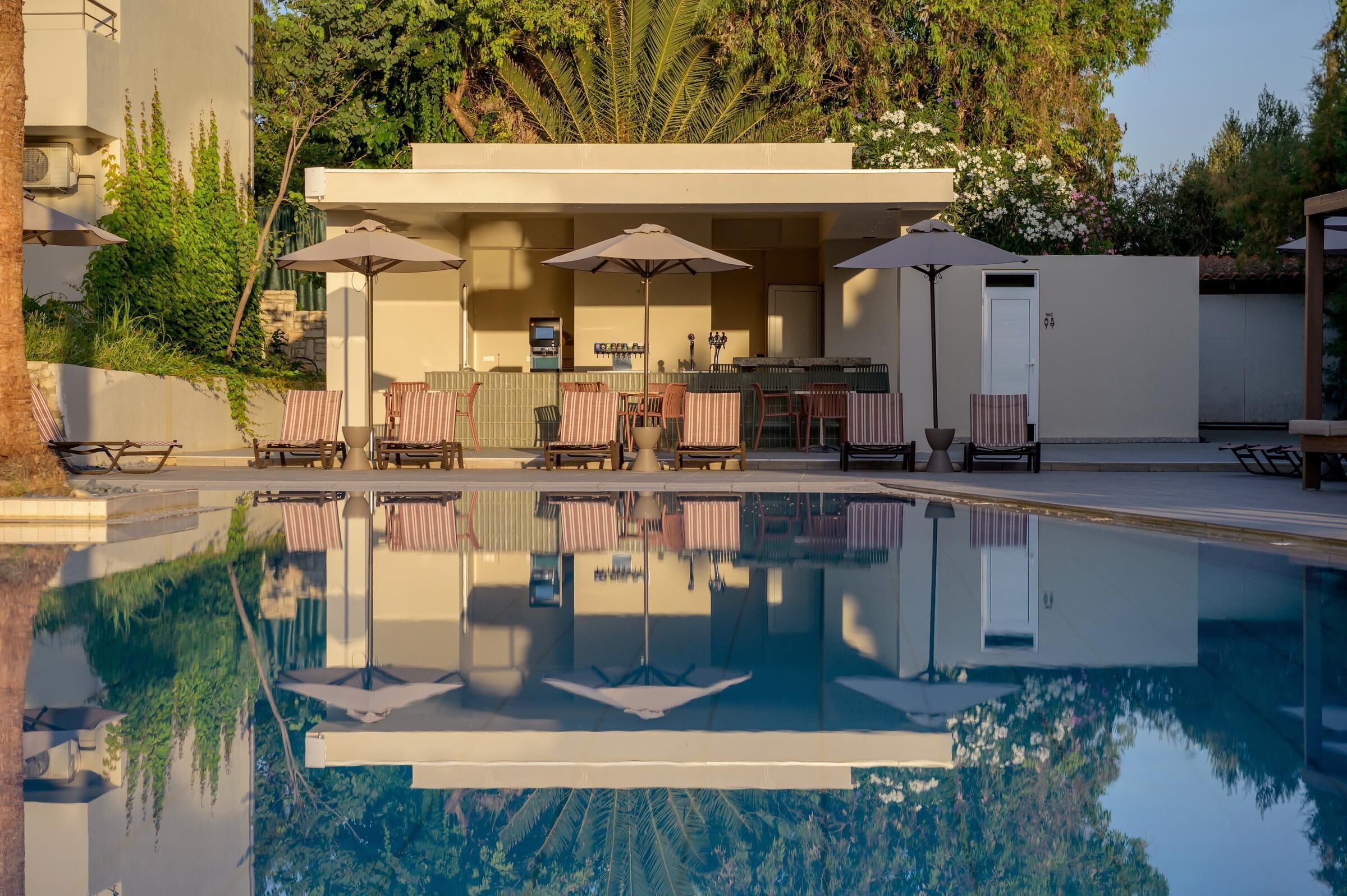Área de piscina com espreguiçadeiras e guarda-sóis, um bar e uma piscina de reflexão.