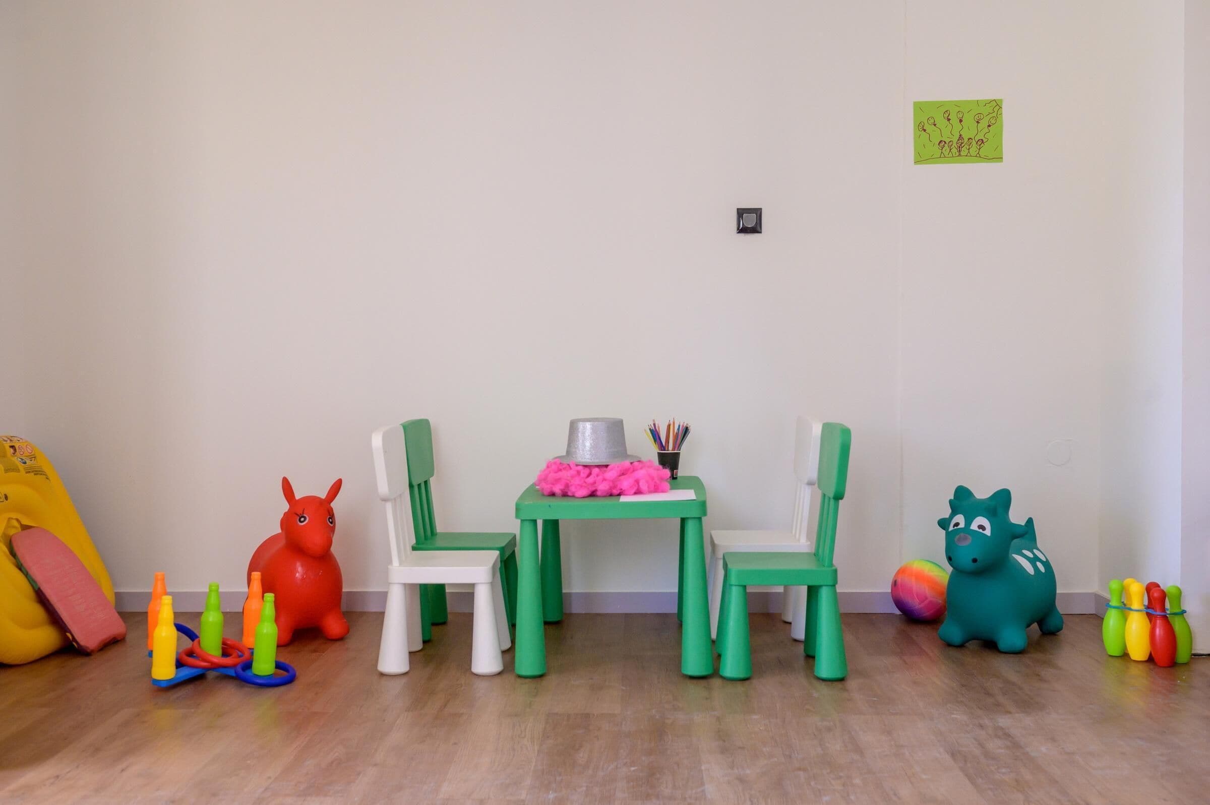 A room with a green table and two green chairs, a red toy, a green toy, and a yellow toy.