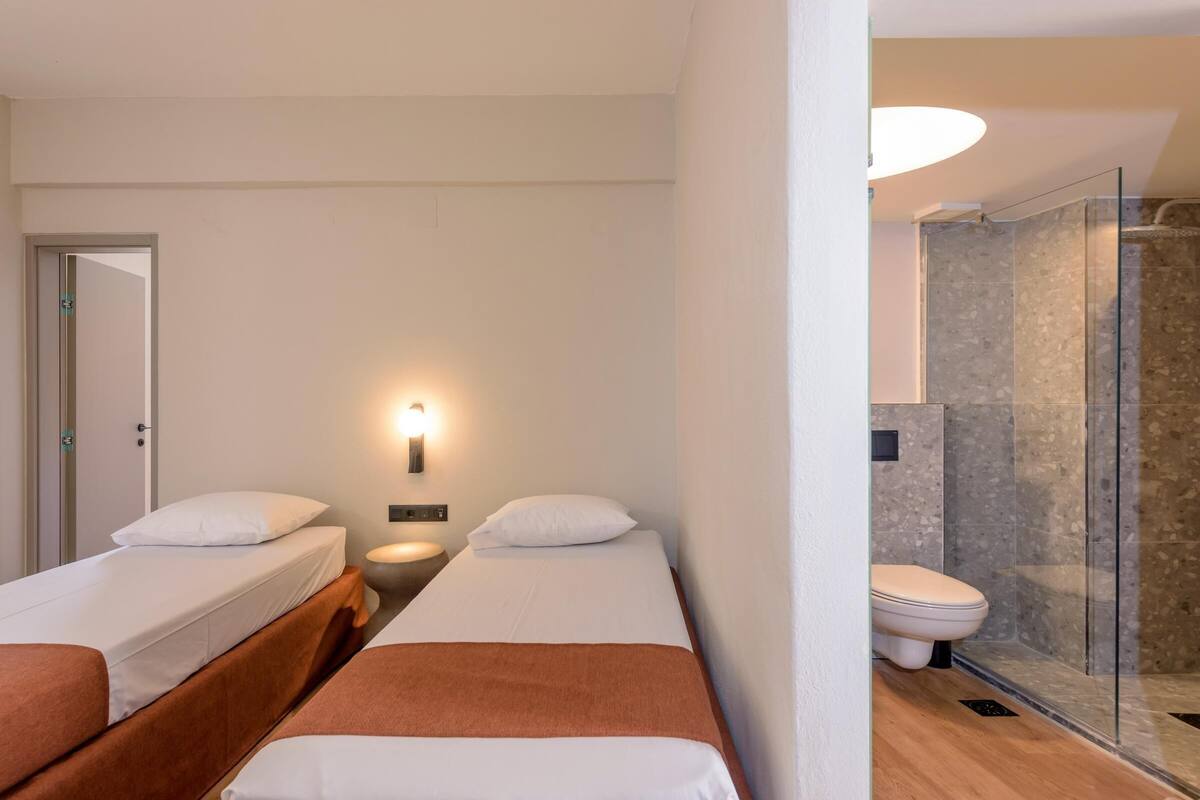 A hotel room with two beds, a shower, and a toilet.