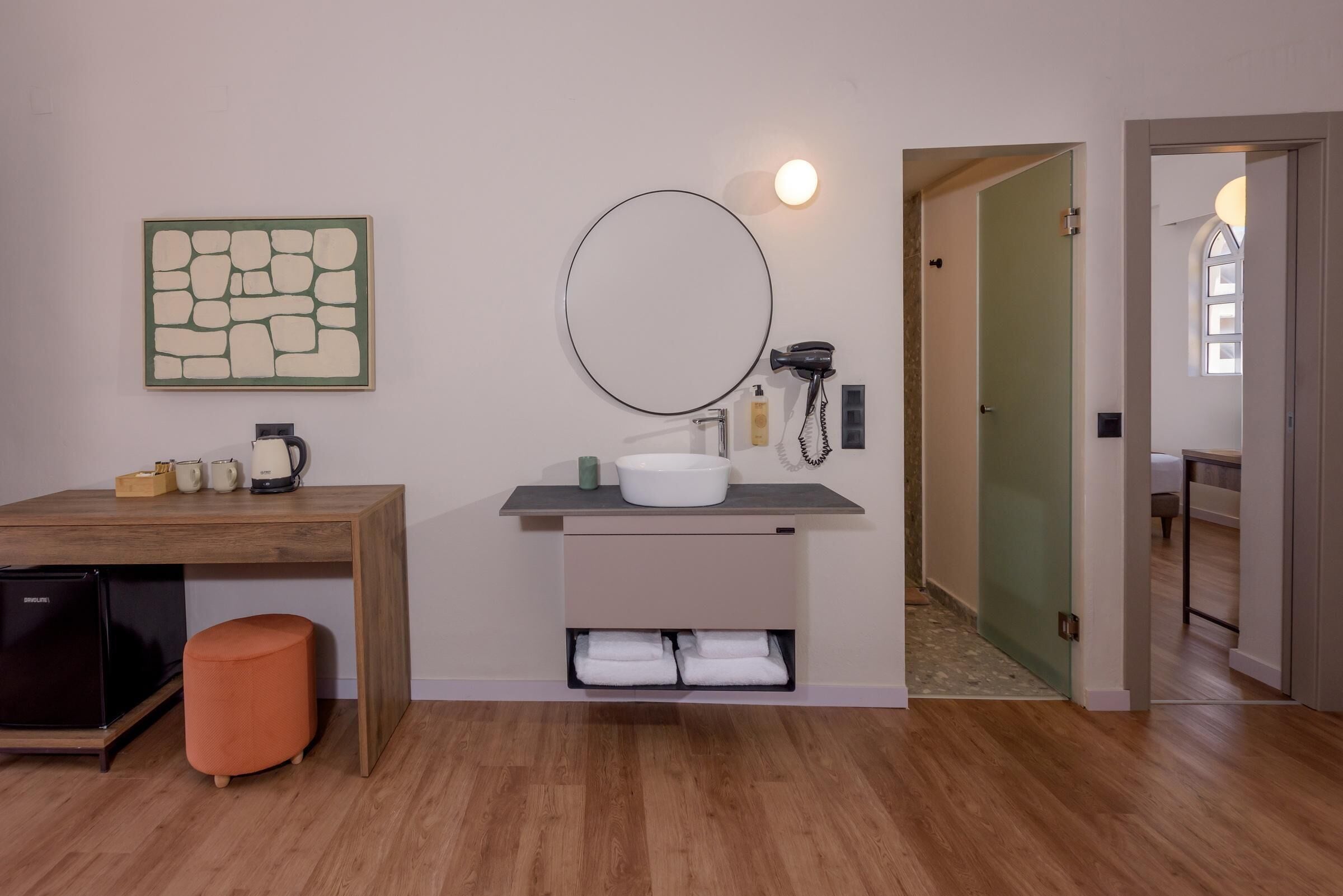 A modern bathroom with a wooden vanity, a round mirror, a sink, and a towel rack.
