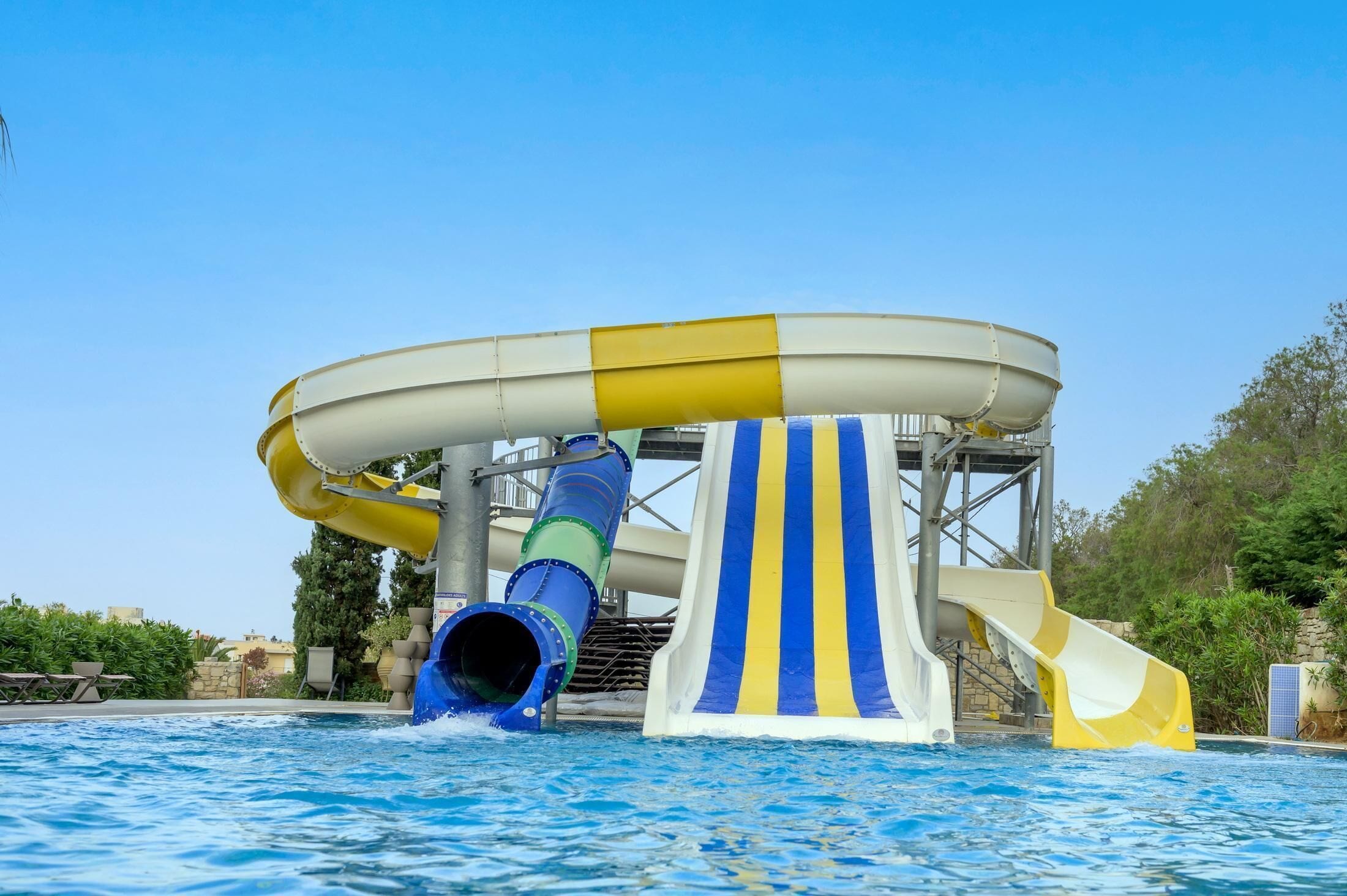 A water park with a large water slide, a pool, and surrounding greenery.