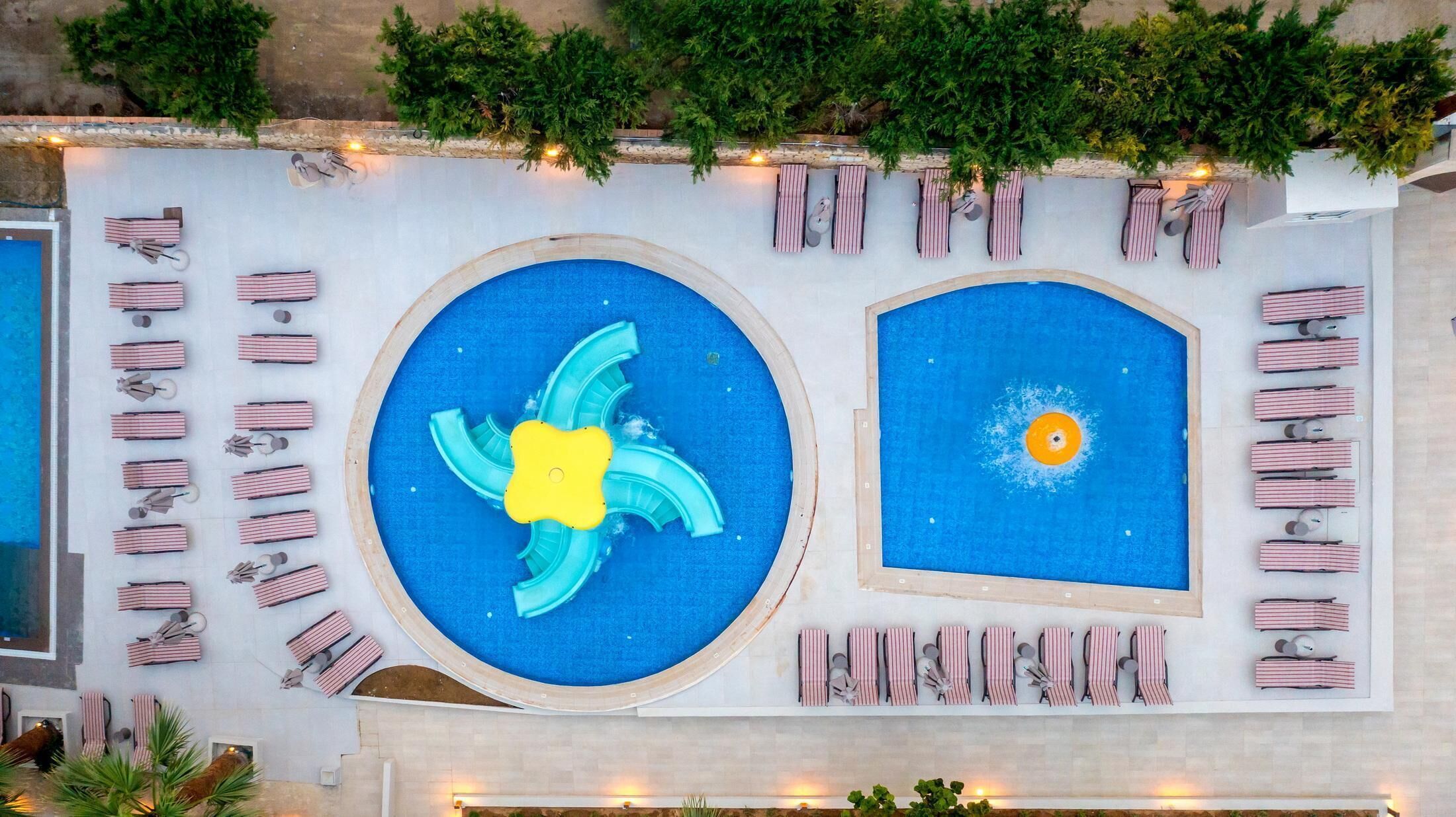 A rooftop pool area with two pools, lounge chairs, and potted plants.
