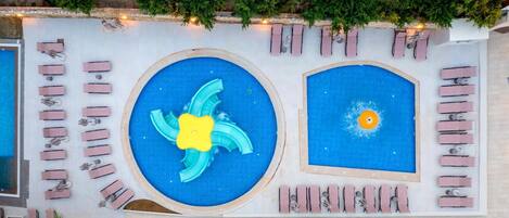 A rooftop pool area with two pools, lounge chairs, and potted plants.