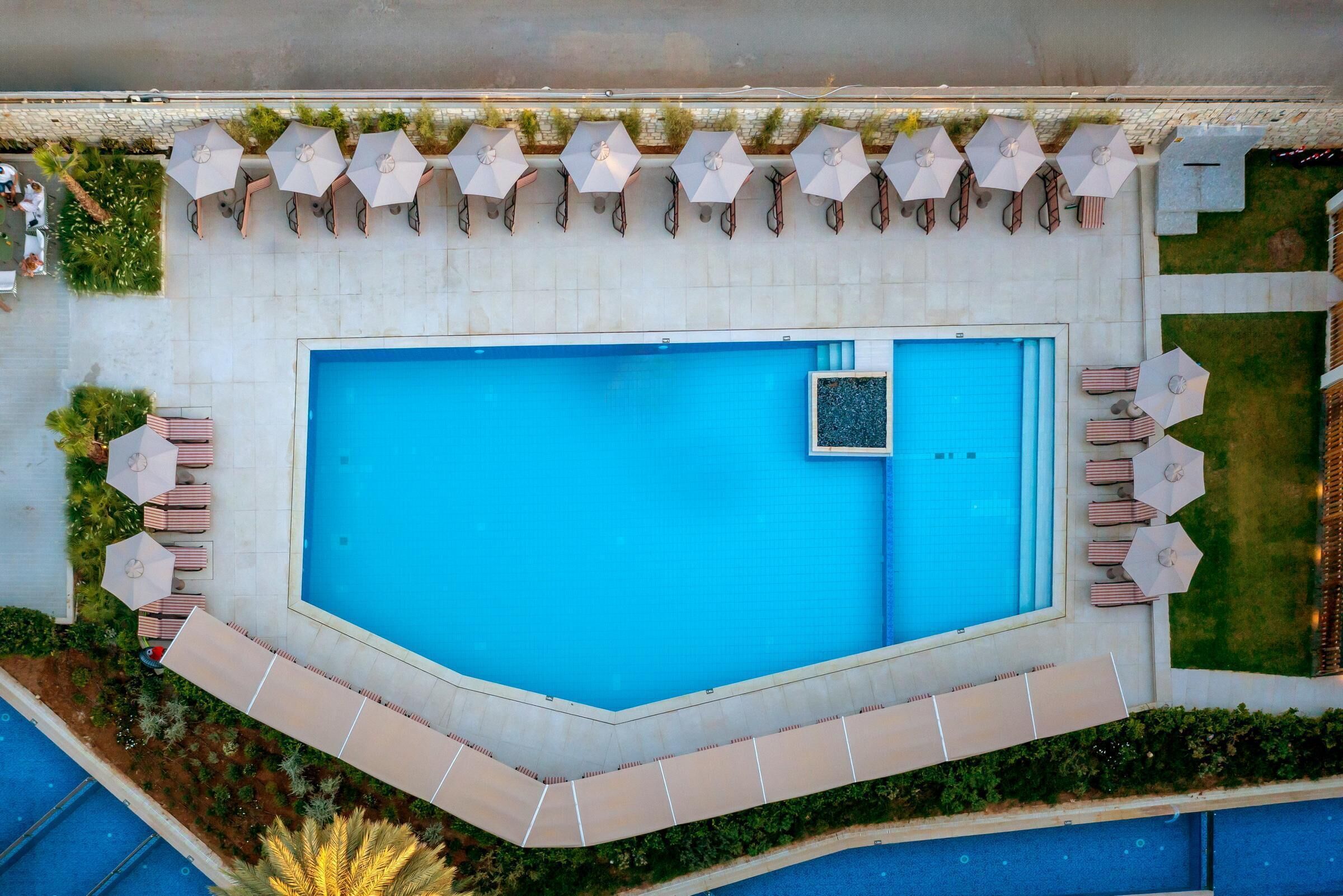 An aerial view of a rectangular swimming pool with surrounding lounge areas, including umbrellas and seating.
