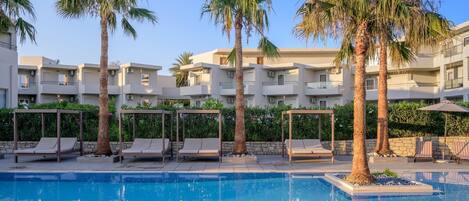 A swimming pool with lounge chairs and palm trees, surrounded by a multi-story building with balconies.