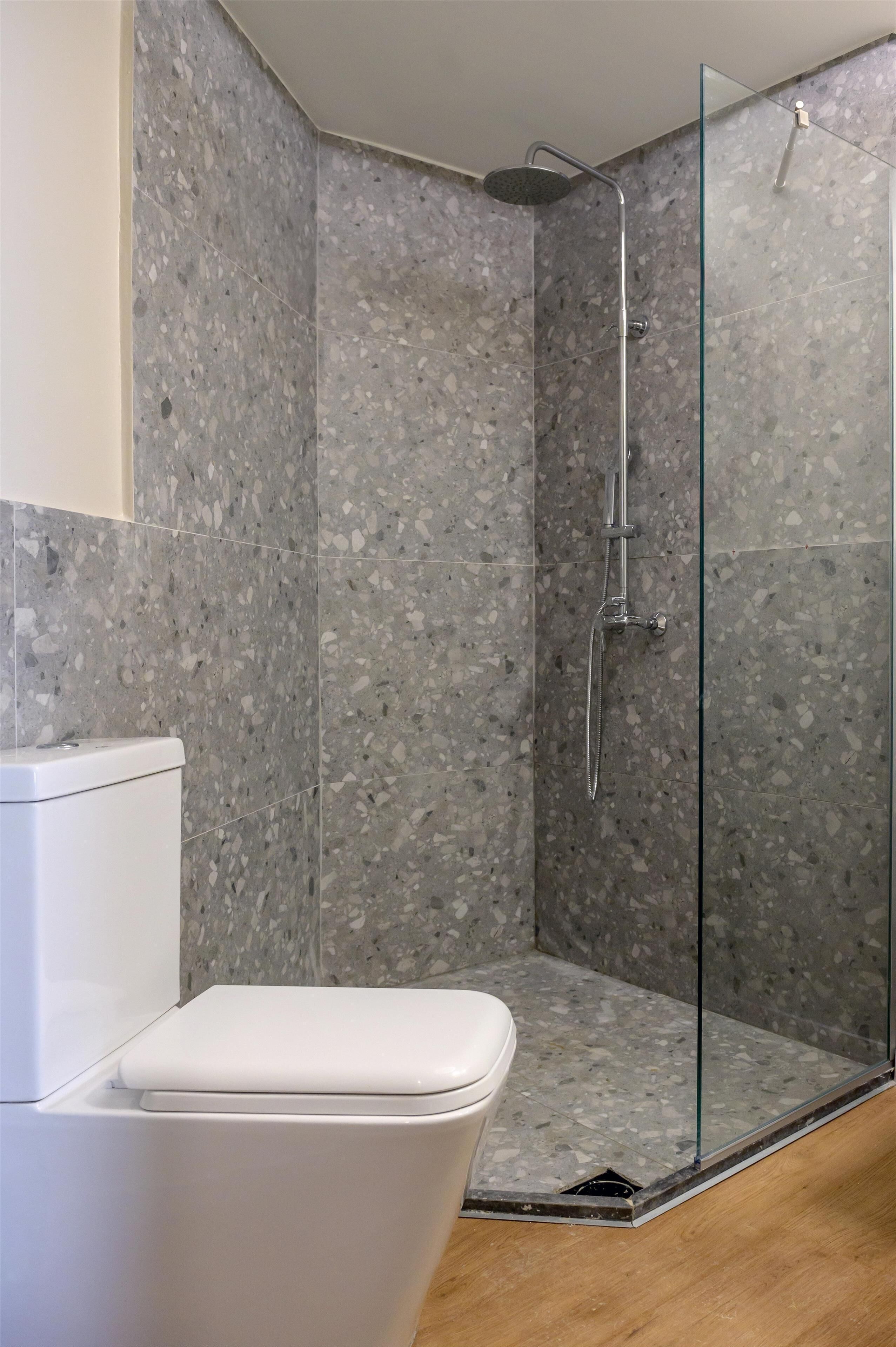 Un baño con ducha de vidrio, inodoro blanco y suelo de terrazo.