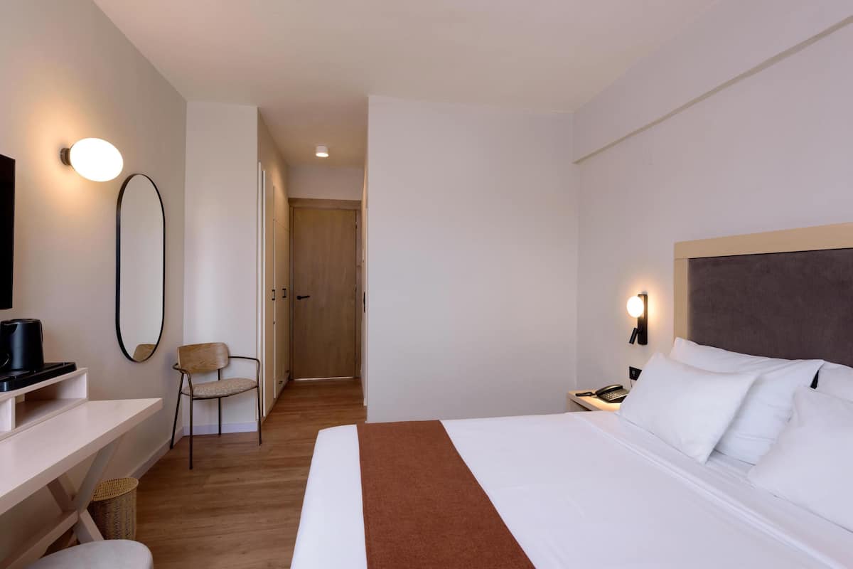 A hotel room with a bed, bedside table, chair, desk, and a TV.