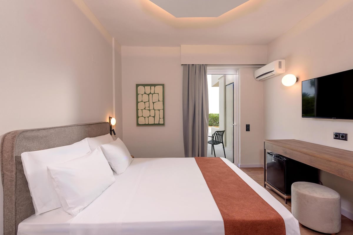 A hotel room with a bed, a TV, a desk, and an air conditioning unit.