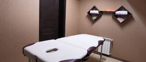 A medical examination room with a treatment table, a door, and two shelves with towels.