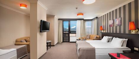 Une chambre d’hôtel avec un lit, un canapé, une télévision, un bureau et une fenêtre donnant sur les montagnes.