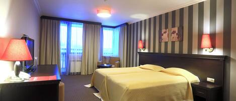 Een hotelkamer met twee bedden, een bureau met lamp, een stoel, een nachtkastje en een raam met gordijnen.