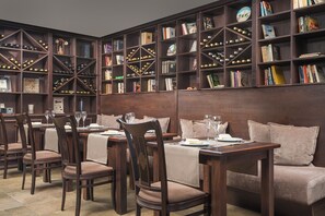A dining area with wooden tables and chairs, surrounded by bookshelves filled with books and wine bottles. - Royal Park Hotel and Apartments (Bansko)