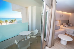 A balcony with a view of the beach, a seating area with a table and chairs, and a bedroom with a bed and a sofa. - Hotel HL Sahara Playa (San Bartolomé de Tirajana)