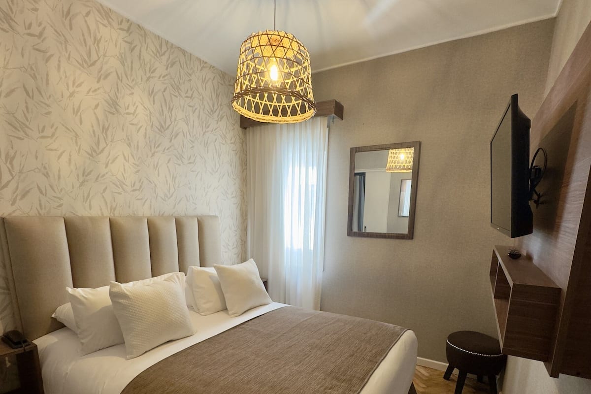 A bedroom with a large bed, a hanging light fixture, a mirror, and a wooden floor.