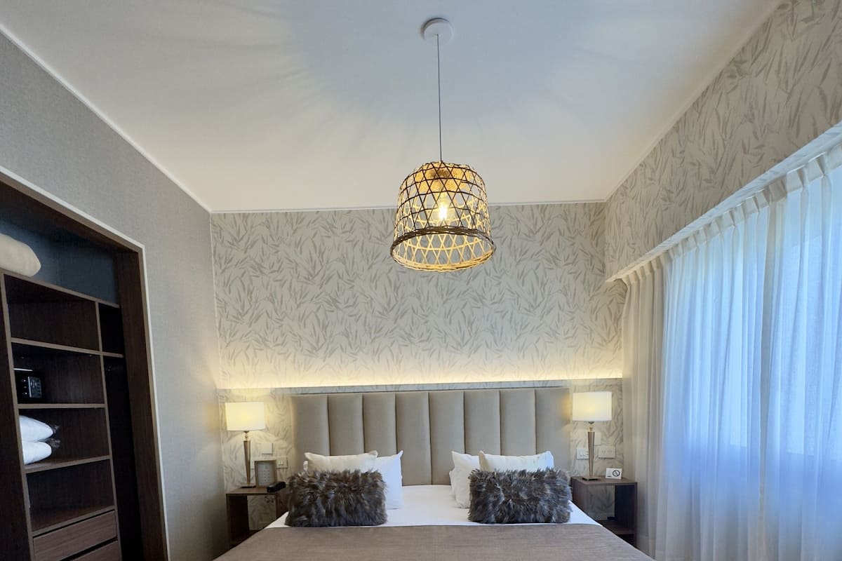 A modern bedroom with a large bed, a bench, a wardrobe, and a ceiling light fixture.