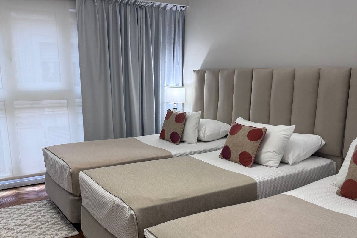 A hotel room with two beds, a large window with curtains, a wooden floor, and a rug.