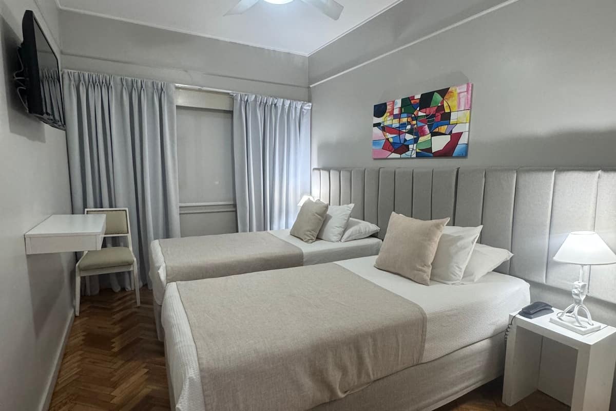 A modern hotel room with two beds, a desk, a chair, a TV, and a ceiling fan.
