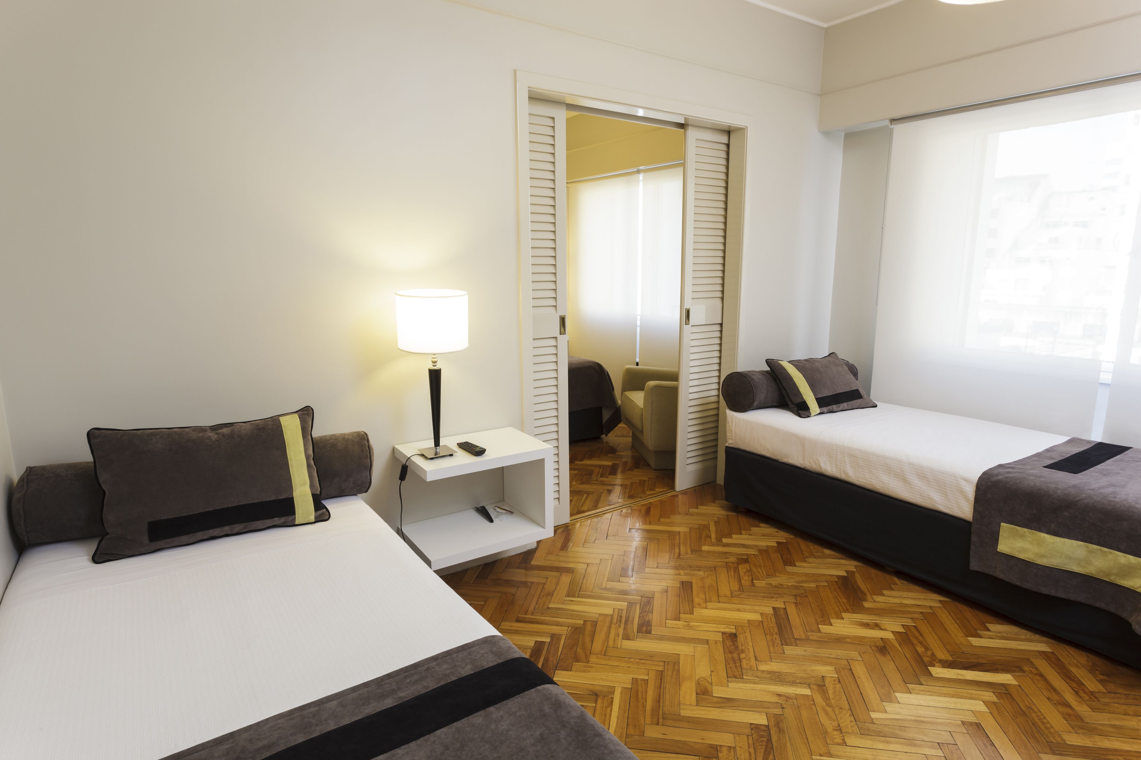 Una habitación de hotel con dos camas, un escritorio con lámpara y un armario.