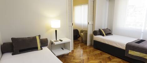 Una habitación de hotel con dos camas, un escritorio con lámpara y un armario.
