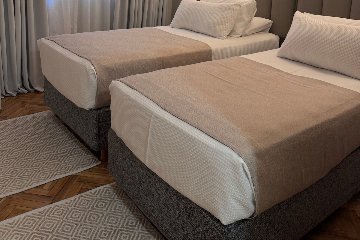 A hotel room with two beds, a headboard, and a patterned rug.