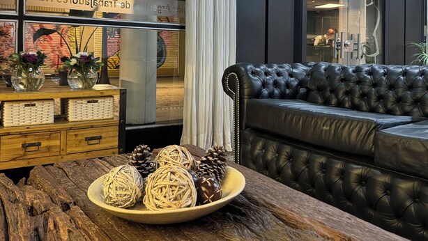 Una sala de estar moderna con un sofá de cuero, una mesa de centro de madera con objetos decorativos, y un ventanal con cortinas.