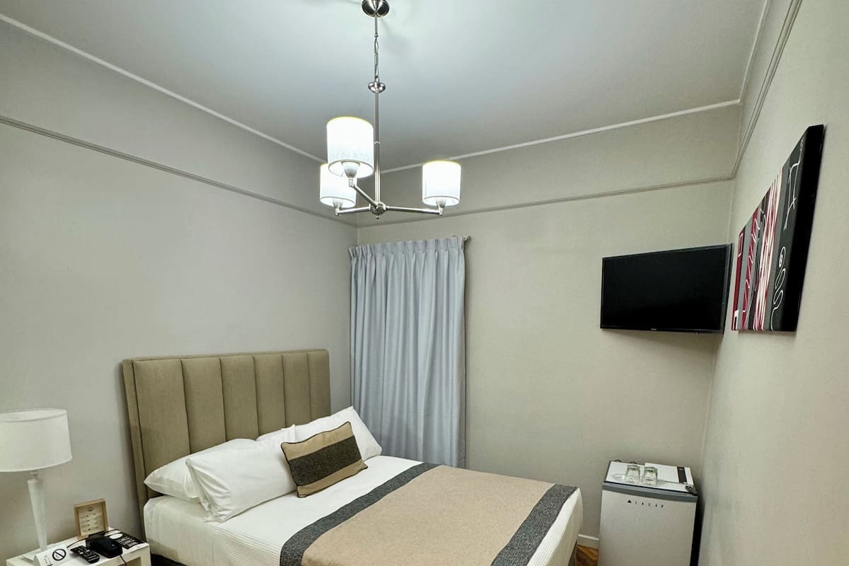 A hotel room with a bed, a desk with a lamp, a television, and a minibar.