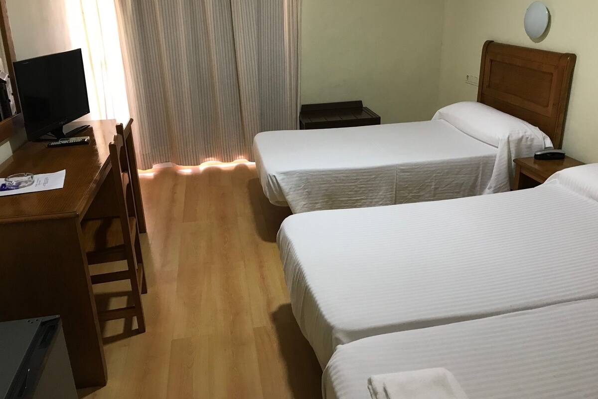 A hotel room with two beds, a desk with a computer, a chair, and a window with curtains.