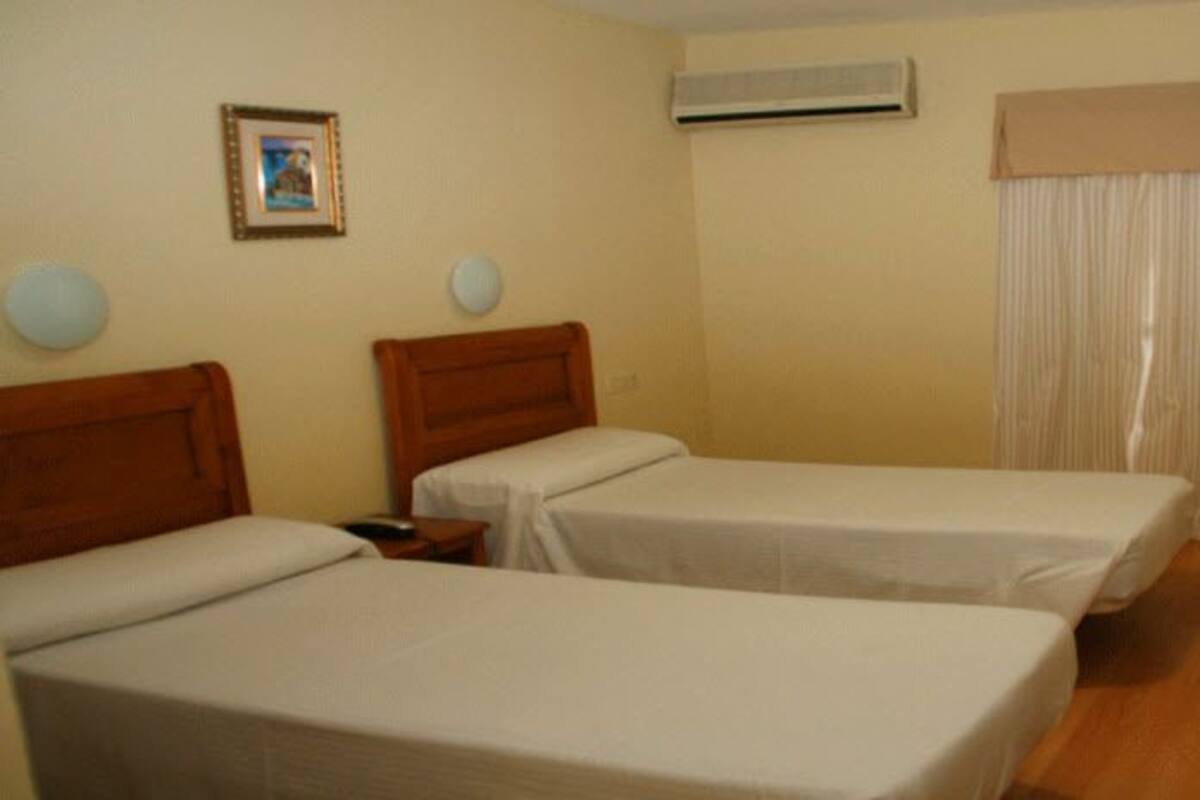 A hotel room with two single beds, a desk with a chair, a television, and a window with curtains.
