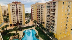 A high-rise residential building with multiple balconies, a swimming pool, and palm trees. - Las Gondolas Apartments (San Javier)