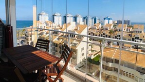 A balcony with a wooden table and chairs, overlooking a coastal cityscape with buildings and the sea. - Las Gondolas Apartments (San Javier)